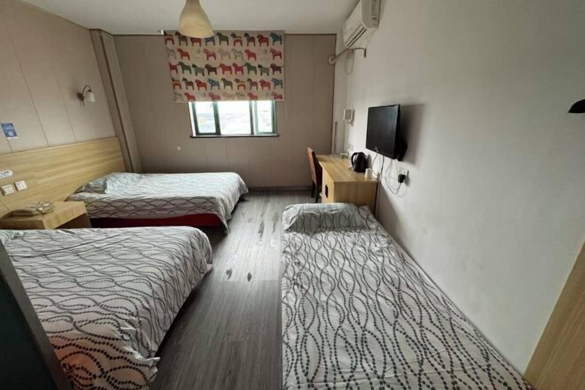Ett hotellrum med två separata sängar, ett skrivbord i trä, en stol, en tv och ett fönster med en mönstrad gardin.