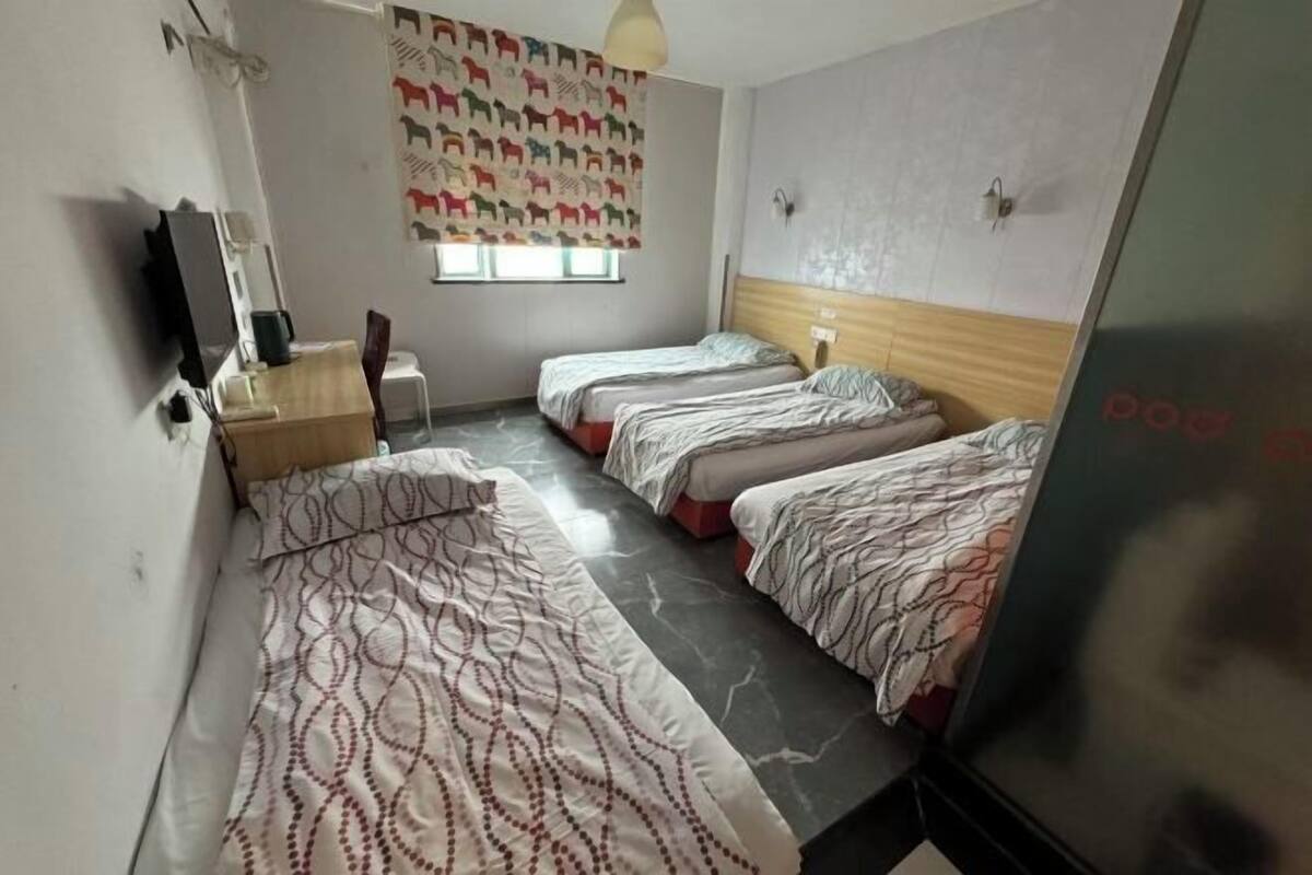 Ett hotellrum med två sängar, ett skrivbord, en stol, en tv och ett fönster med mönstrade gardiner.