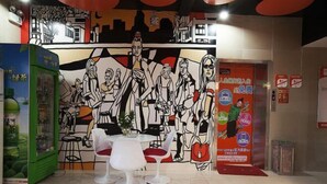 A dining area with a mural, white chairs, and a green vending machine. - Dingding Hotel (Shanghai Pudong Airport Heqing Town) (Shanghai)