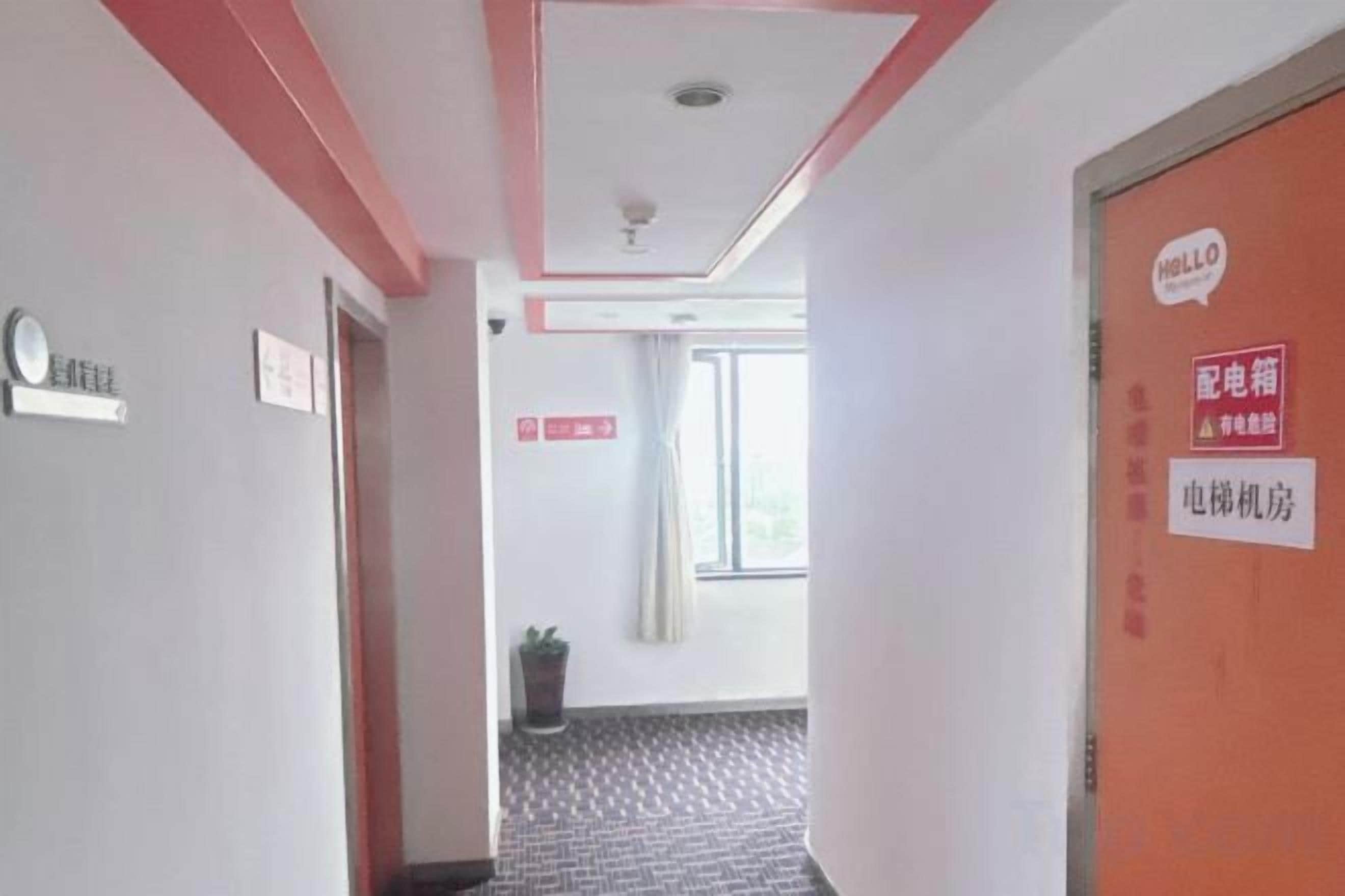 Ein Hotelkorridor mit einer roten Tür, einem Schild, das den Zimmertyp angibt, und einem Fenster mit Vorhängen.