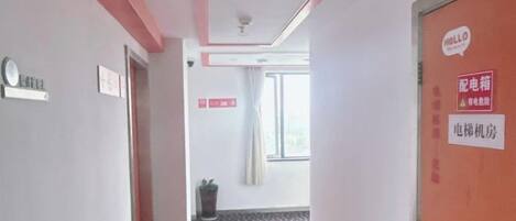 Ein Hotelkorridor mit einer roten Tür, einem Schild, das den Zimmertyp angibt, und einem Fenster mit Vorhängen.
