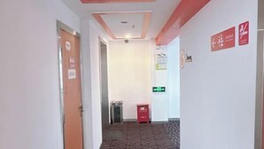 A hallway with a patterned carpet, a door with a sign, a trash bin, and directional signs on the wall. - Dingding Hotel (Shanghai Pudong Airport Heqing Town) (Shanghai)