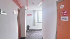 A hotel hallway with a patterned carpet, a ceiling light, a potted plant, and a door with a 'HELLO' sign. - Dingding Hotel (Shanghai Pudong Airport Heqing Town) (Shanghai)