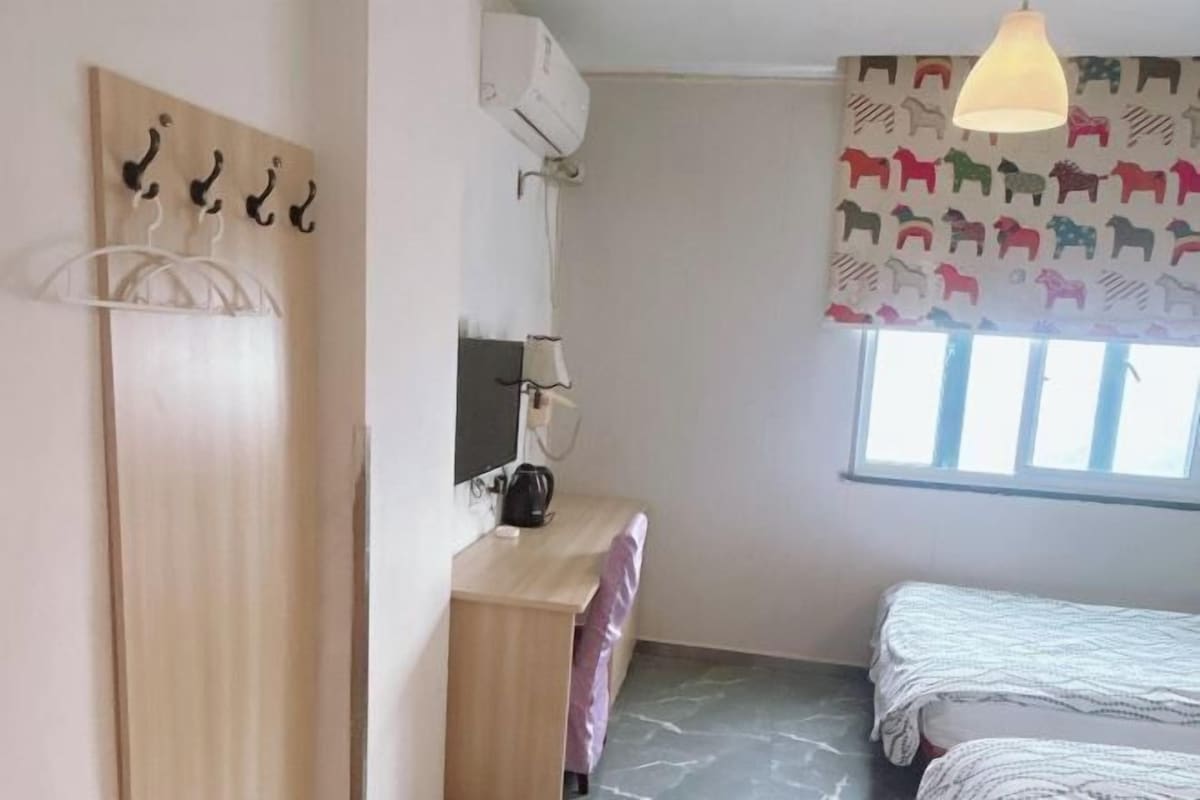 Una camera da letto con un letto, una scrivania, una sedia, un armadio, una lampada a sospensione e una finestra con tenda.