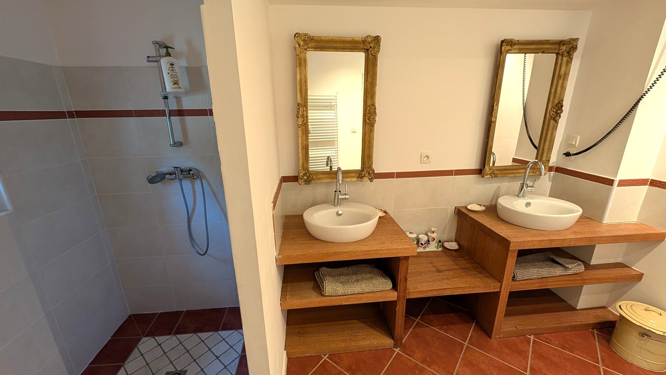 Une salle de bain avec deux lavabos, une douche et un meuble-lavabo avec des étagères.
