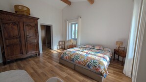 A bedroom with a wooden wardrobe, a bed with a colorful floral bedspread, a wooden chair, and a small table with a lamp. - Domaine de la Pigne, tranquillity as far as the eye can see (Puy-Saint-Martin)