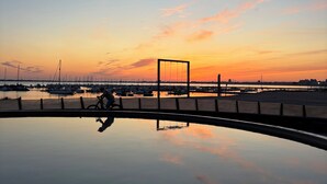 A calm marina at sunset with boats docked and a person cycling.