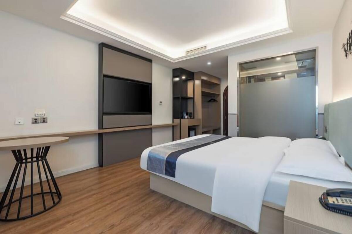 A modern hotel room with a bed, bedside table, and a flat-screen TV mounted on the wall.