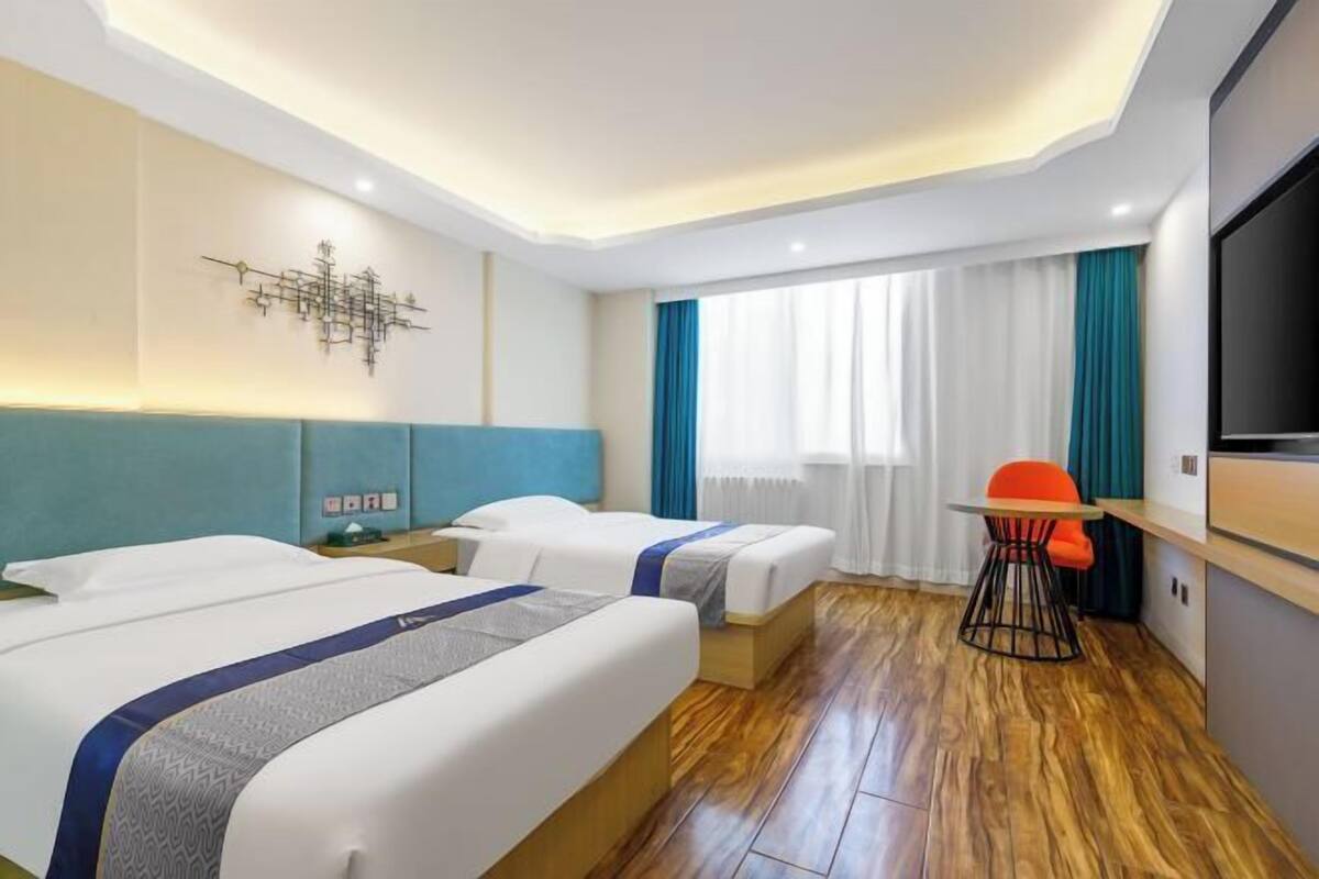 A hotel room with two beds, a desk, a chair, a TV, and a window with curtains.