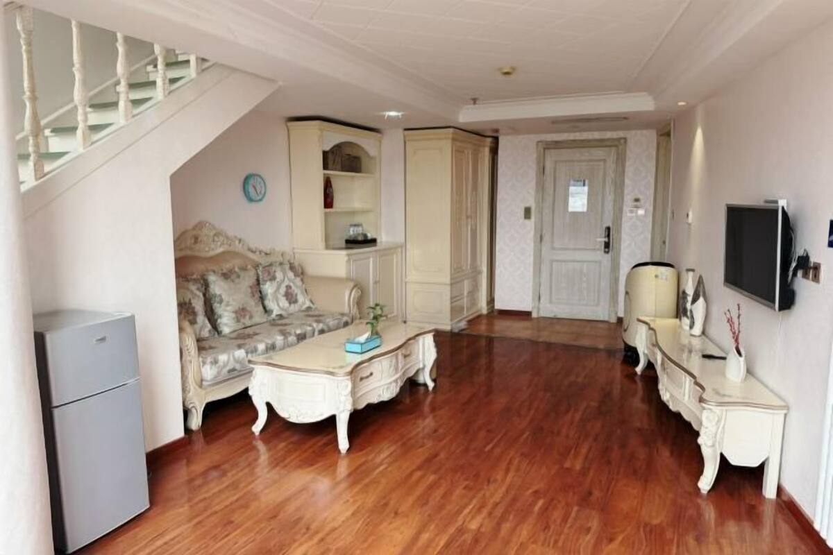 A spacious living area with a sofa, a coffee table, a TV, and a refrigerator.