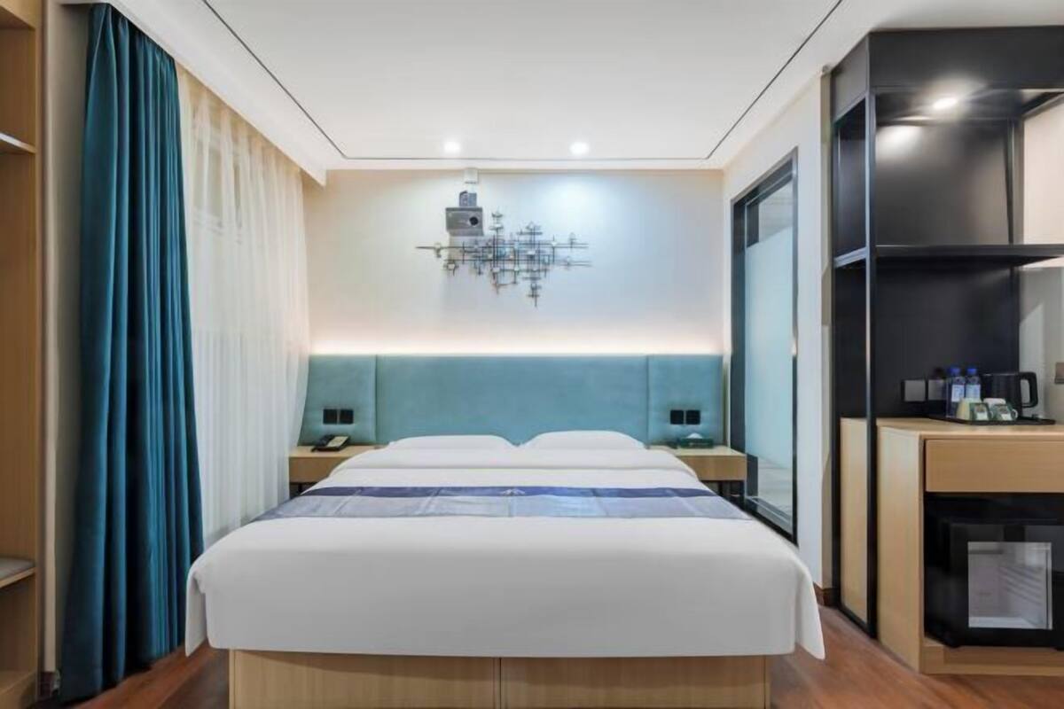 A hotel room with a bed, two bedside tables, a wall-mounted light fixture, and a built-in TV.