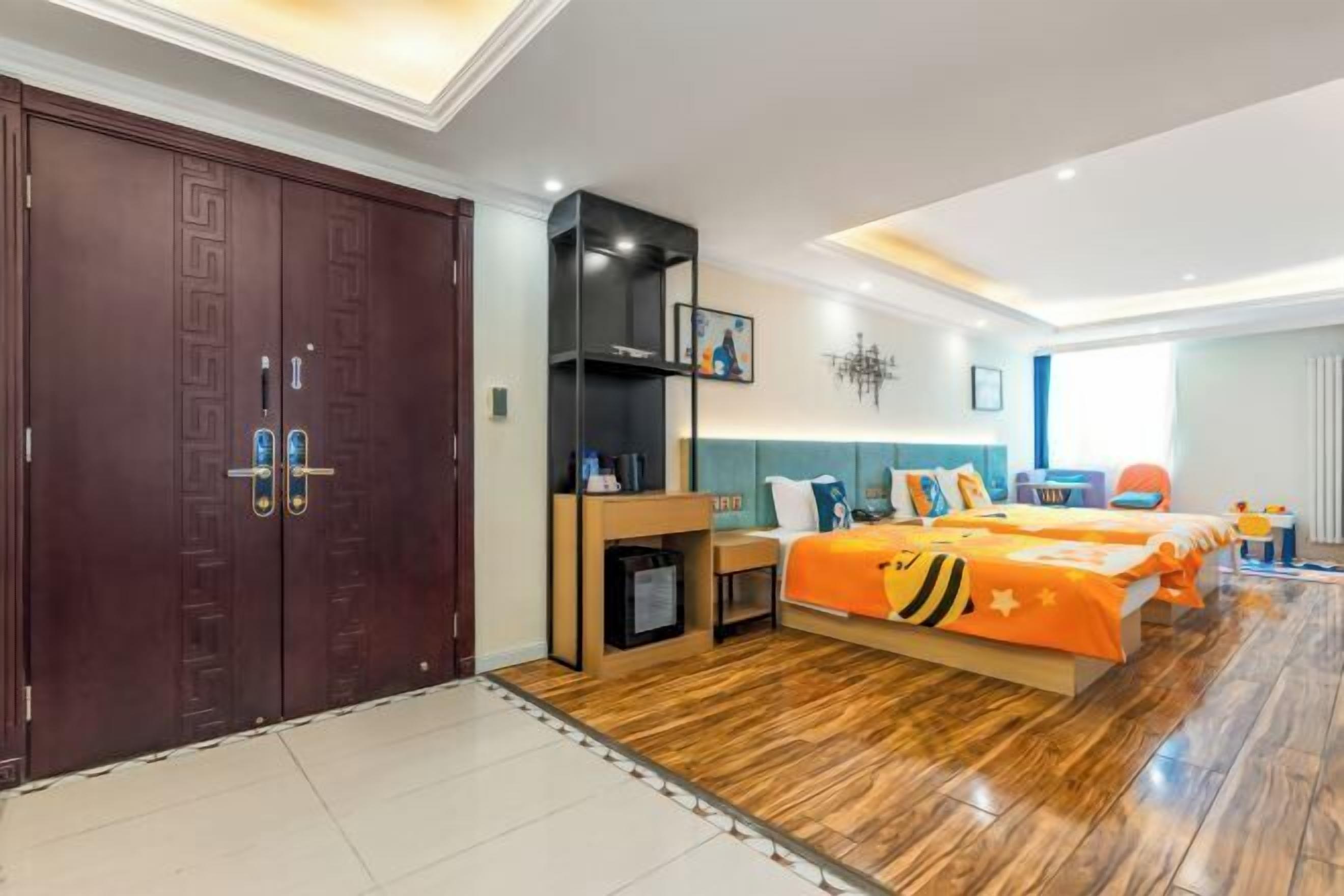 A hotel room with a large wardrobe, a bed with an orange bedspread, a bedside table, and a small desk.