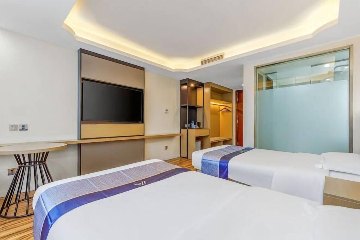 A hotel room with two beds, a TV, a small table, and a glass partition wall.