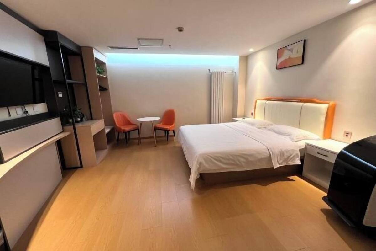 A hotel room with a bed, a desk, two chairs, a TV, and a small table.