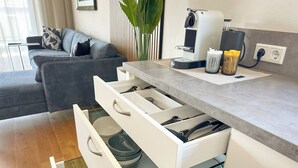 Una cocina moderna con armarios blancos, una cafetera y una zona de comedor con un sofá gris.