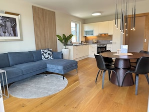A modern kitchen with white cabinets, a wooden dining table, and a blue sofa.