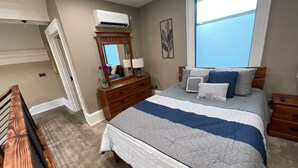 Une chambre avec un grand lit, une commode, un appareil de climatisation et une fenêtre.