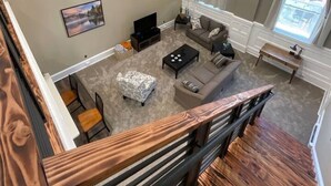 Un salon spacieux avec un plafond haut, une grande fenêtre et un escalier menant à l’étage supérieur.