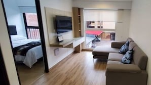 Habitación de hotel moderna con cama, sofá, televisión y vista al exterior.