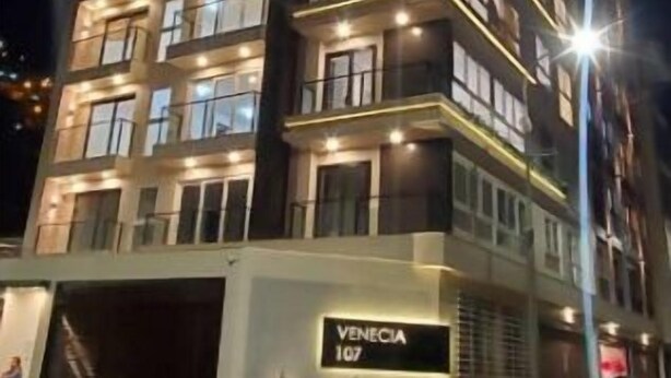 Un hotel de varios pisos con balcones iluminados y un cartel que dice 'VENECIA 107'.