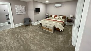 Une chambre à coucher avec un grand lit, une table de chevet, une chaise, un téléviseur et un appareil de climatisation.