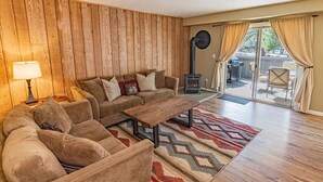Un salon chaleureux avec un mur en bois, un canapé, une table basse et une vue sur l’extérieur grâce à une porte vitrée.