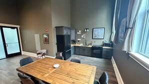 Un vaste espace de vie comprenant un coin repas avec une table en bois, une cuisine à l’arrière-plan et une grande fenêtre agrémentée de rideaux.