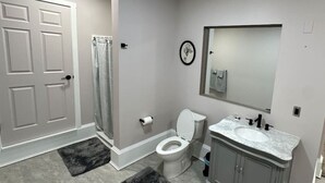Une salle de bain comprenant des toilettes, un lavabo, un meuble-lavabo, une douche et une porte.