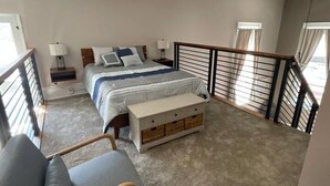 Une chambre à coucher comprenant un lit, des tables de chevet, un banc, une chaise et un balcon avec une balustrade.