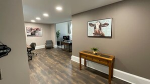 Un couloir doté d’un plancher en bois, d’un bureau agrémenté d’une plante et de tableaux encadrés accrochés aux murs.