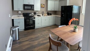 Une cuisine moderne avec des meubles de couleur gris clair, un réfrigérateur noir et une table à manger en bois accompagnée de deux chaises.