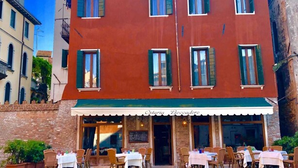 A two-story building with a red facade and green shutters, featuring outdoor seating with tables and chairs. - CA' DI LUNA VENEZIA  (Venice)