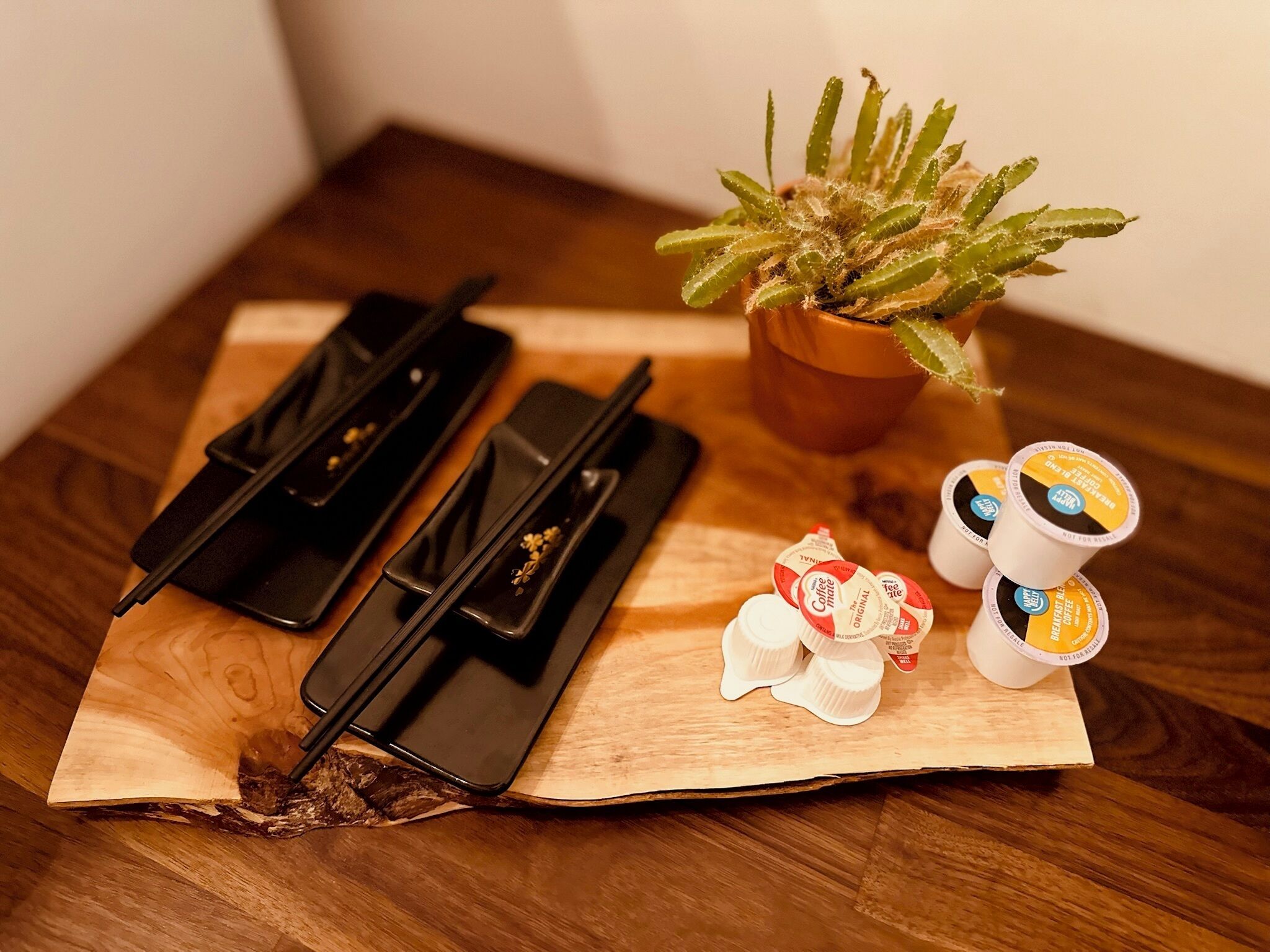 Una mesa de madera con una bandeja negra, una pequeña planta en maceta y una pila de cápsulas de café.