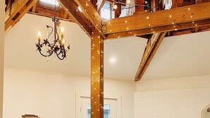 Une pièce spacieuse avec un plafond en bois, un lustre, un mur en briques blanches et un réfrigérateur blanc.