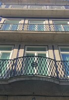 Un edificio de varios pisos con un balcón que tiene barandilla de celosía metálica.