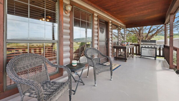 A covered patio with wicker furniture, a grill, and large windows.