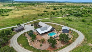 A large house with a swimming pool, surrounded by a landscaped garden and a winding driveway.