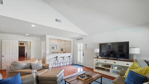 A spacious living room with a large flat-screen TV, leather sofas, and a coffee table.