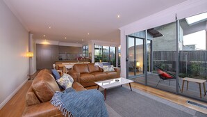 Un salon moderne avec un canapé en cuir, une table basse et une porte vitrée donnant sur un balcon équipé d’une chaise.