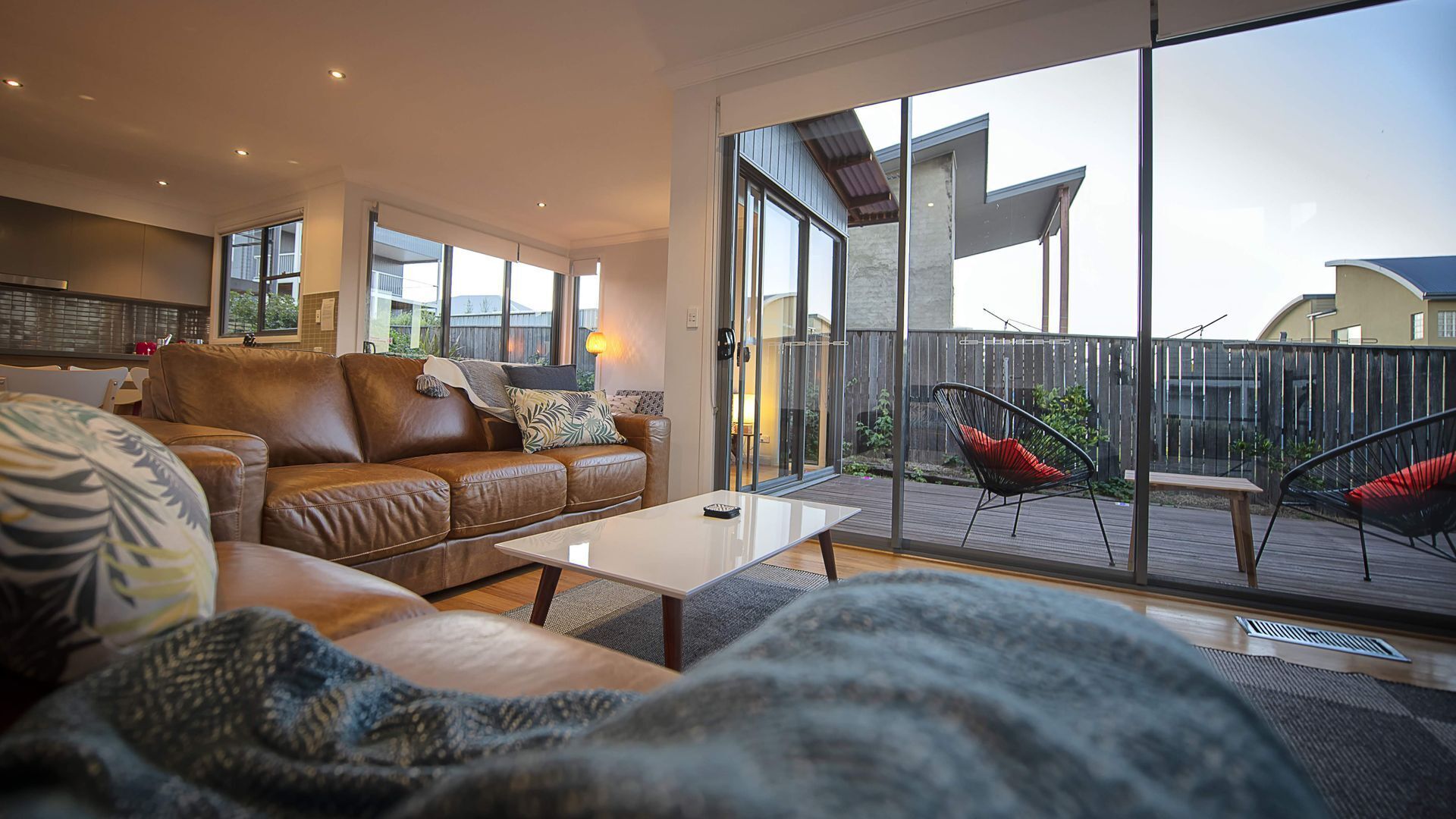 A modern living room with a leather sofa, a coffee table, and a view of a wooden deck with outdoor seating.