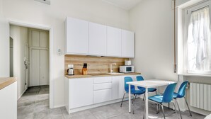 A modern kitchen with white cabinets, a wooden countertop, a microwave, and blue chairs around a white table. - Charming studio near the city centre (Milan)