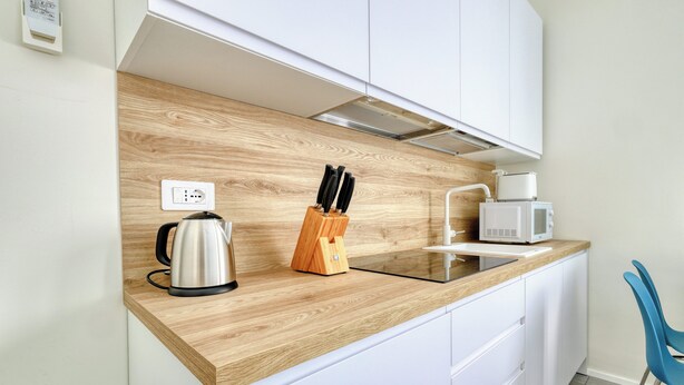 A modern kitchen with a wooden countertop, white cabinets, a kettle, a knife block, a microwave, and a blue chair. - Charming studio near the city centre (Milan)