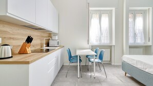 A modern kitchen with white cabinets, a wooden countertop, and a kettle. There is a dining area with a white table and blue chairs. - Charming studio near the city centre (Milan)