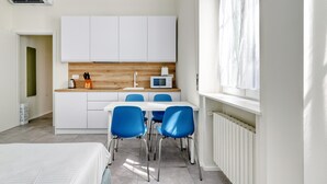 A modern kitchen with white cabinets, a wooden countertop, and a microwave. There is a dining area with a white table and blue chairs. - Charming studio near the city centre (Milan)