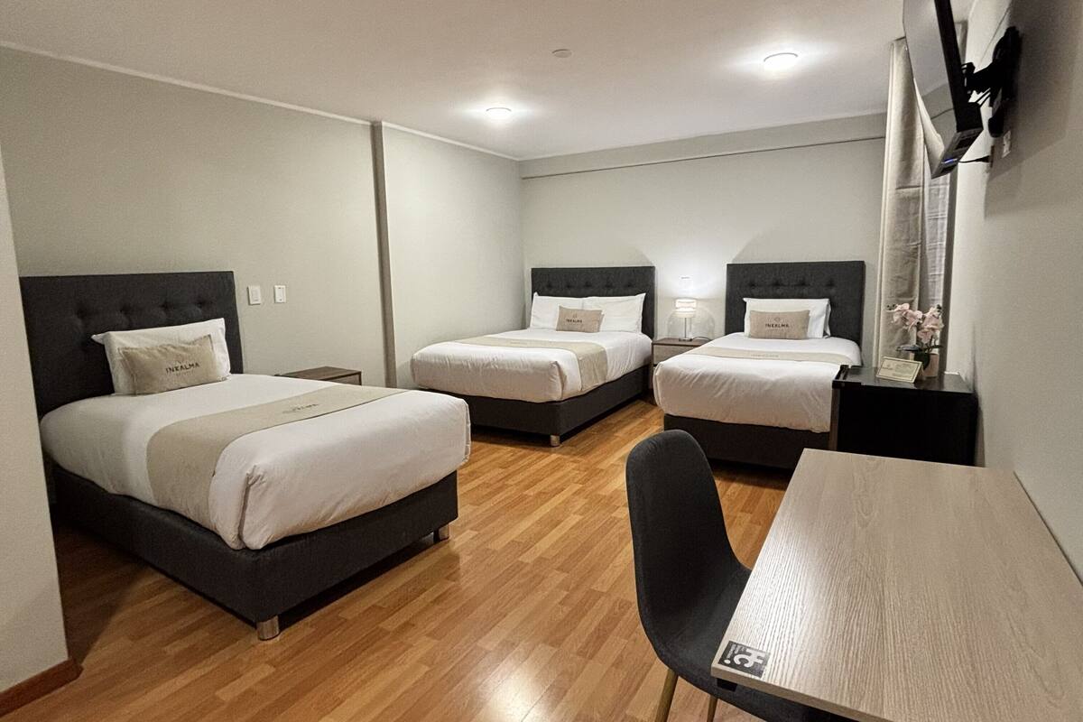 A hotel room with three beds, a desk, and a chair.