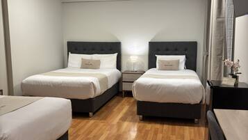 A hotel room with two beds, a desk, a chair, a nightstand, a lamp, and a mirror.