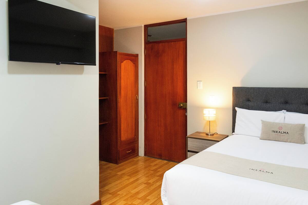A hotel room with a bed, a TV, a wardrobe, and a nightstand with a lamp.