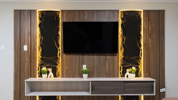 A modern living room with a flat-screen TV mounted on a wooden wall with decorative lighting, a white console table with decorative items, and a wooden coffee table. - HOTEL INKALMA SANTA MARTA (Arequipa)