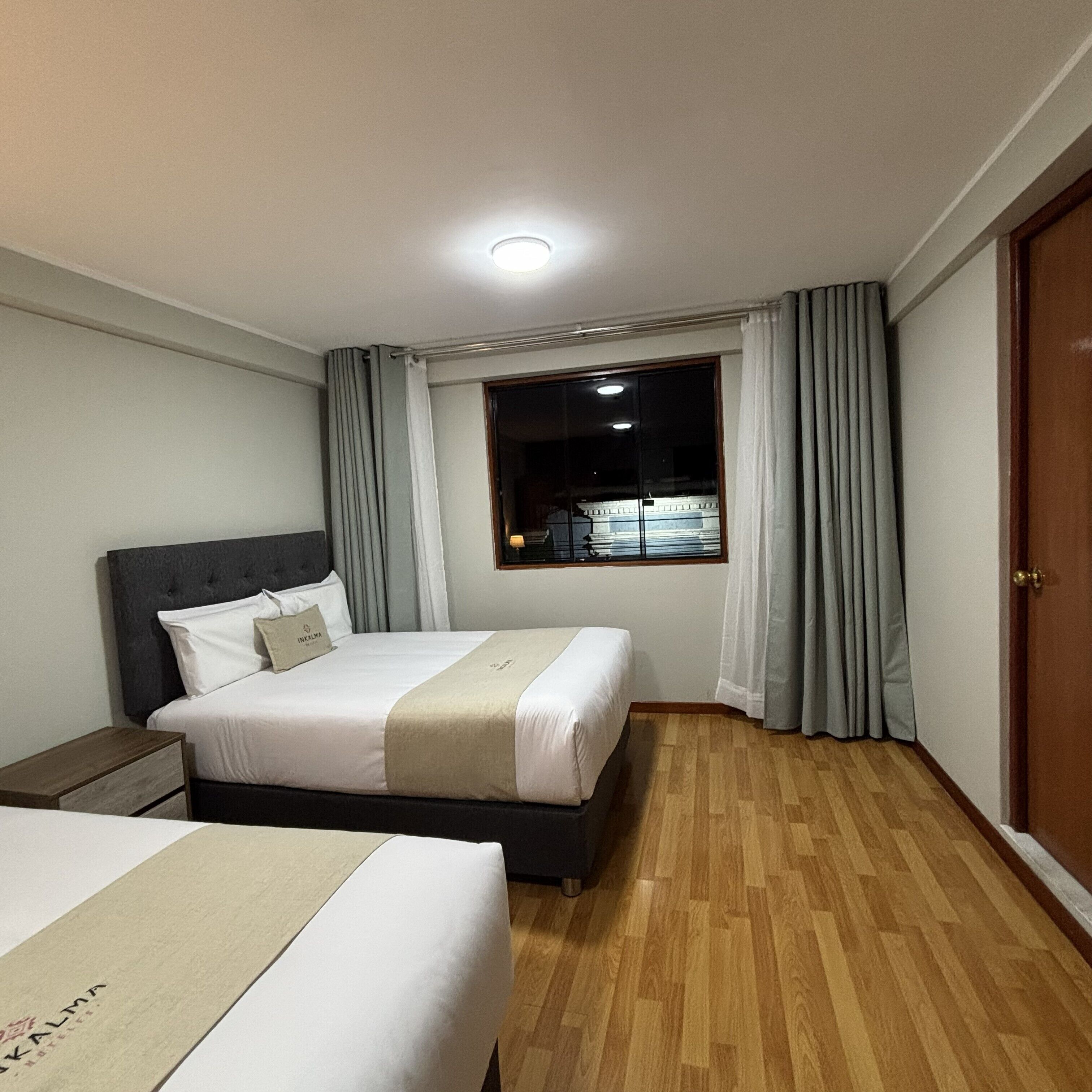 A hotel room with a bed, a nightstand, a window with curtains, and a door.