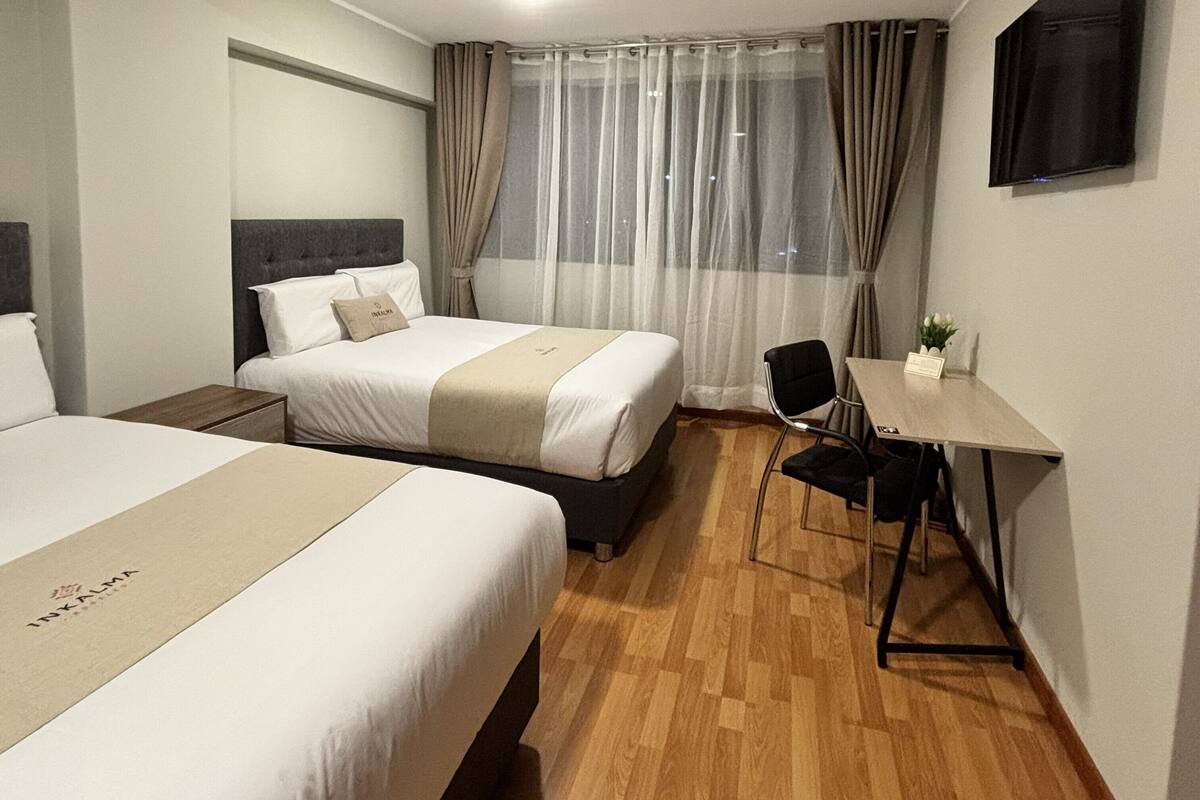 A hotel room with two beds, a desk, a chair, a TV, and a window with curtains.